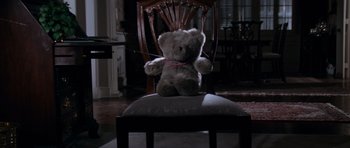Movie still from “Cape Fear” (1991), directed by Martin Scorsese – A teddy bear sitting on top of an ottoman in a living room; Medium shot, Overhead angle