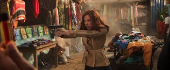 Movie still from “Captain America: Civil War” (2016), directed by Anthony Russo – A woman holding a gun while standing in a room full of clothes; Medium shot, Over the shoulder angle
