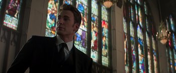 Movie still from “Captain America: Civil War” (2016), directed by Anthony Russo – A man wearing a suit and tie in front of a stained glass window; Close Up shot, Low angle