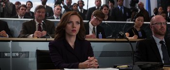 Movie still from “Captain America: Civil War” (2016), directed by Anthony Russo – A woman sitting at a table in front of a group of people; Medium shot, Over the shoulder angle