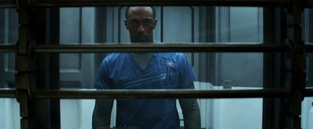 Movie still from “Captain America: Civil War” (2016), directed by Anthony Russo – A man in a blue shirt behind bars looking at the camera; Medium shot, Over the shoulder angle