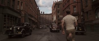Movie still from “Captain America: The First Avenger” (2011), directed by Joe Johnston – A man walking down a street past a building; Wide shot, Over the shoulder angle