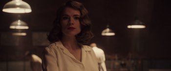 Movie still from “Captain America: The First Avenger” (2011), directed by Joe Johnston – A woman in a white shirt is standing in a dimly - lit room; Close Up shot, Over the shoulder angle