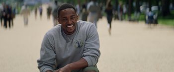 Movie still from “Captain America: The Winter Soldier” (2014), directed by Anthony Russo – A man sitting on the ground smiling for the camera; Close Up shot, Over the shoulder angle