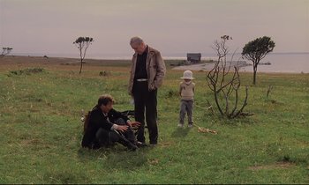 Movie still from “The Sacrifice” (1986), directed by Andrei Tarkovsky – Two men and a child in a field; Wide shot, Low angle