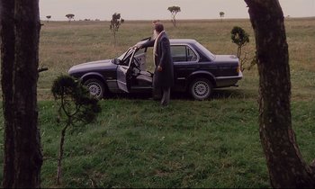 Movie still from “The Sacrifice” (1986), directed by Andrei Tarkovsky – A man standing next to a car in a grassy field; Wide shot, High angle