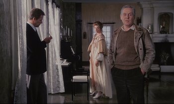 Movie still from “The Sacrifice” (1986), directed by Andrei Tarkovsky – Two men and a woman standing in front of a piano; Medium shot, Over the shoulder angle