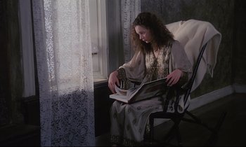 Movie still from “The Sacrifice” (1986), directed by Andrei Tarkovsky – A woman sitting in a chair reading a magazine; Medium shot, High angle