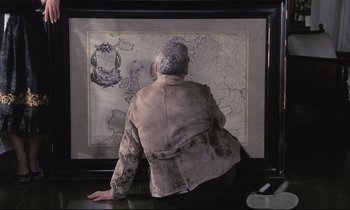 Movie still from “The Sacrifice” (1986), directed by Andrei Tarkovsky – An older man sitting in front of a map; Medium shot, High angle