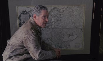 Movie still from “The Sacrifice” (1986), directed by Andrei Tarkovsky – A man sitting in front of a map of europe; Medium shot, High angle