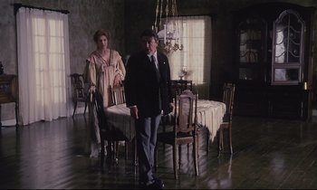 Movie still from “The Sacrifice” (1986), directed by Andrei Tarkovsky – A man and a woman standing in front of a dining room table; Wide shot, High angle