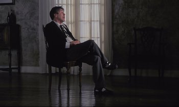 Movie still from “The Sacrifice” (1986), directed by Andrei Tarkovsky – A man in a suit sitting in a chair in front of a window; Wide shot, Low angle