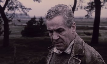Movie still from “The Sacrifice” (1986), directed by Andrei Tarkovsky – An older man in a brown jacket is standing in a field; Close Up shot, Low angle