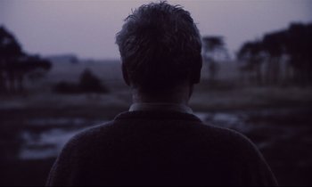 Movie still from “The Sacrifice” (1986), directed by Andrei Tarkovsky – A man is looking out over a field at dusk; Close Up shot, Over the shoulder angle