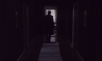 Movie still from “The Sacrifice” (1986), directed by Andrei Tarkovsky – A person walking down a hallway in a dark room; Wide shot, Low angle
