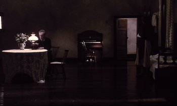 Movie still from “The Sacrifice” (1986), directed by Andrei Tarkovsky – A man sitting at a table in front of an organ; Wide shot, High angle