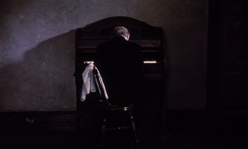 Movie still from “The Sacrifice” (1986), directed by Andrei Tarkovsky – An old man standing in front of a piano; Wide shot, High angle