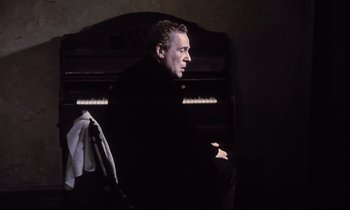 Movie still from “The Sacrifice” (1986), directed by Andrei Tarkovsky – A man sitting on top of an upright piano; Medium shot, Low angle