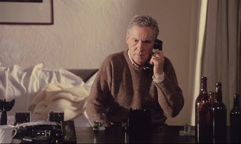 Movie still from “The Sacrifice” (1986), directed by Andrei Tarkovsky – An older man sitting at a table talking on a cell phone; Medium shot, High angle
