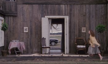 Movie still from “The Sacrifice” (1986), directed by Andrei Tarkovsky – An open door leading to an old barn with a car parked in it; Wide shot, High angle