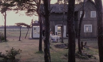Movie still from “The Sacrifice” (1986), directed by Andrei Tarkovsky – Two people sitting at a table in front of a house; Extreme Wide shot, High angle