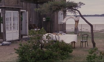 Movie still from “The Sacrifice” (1986), directed by Andrei Tarkovsky – An outdoor dining area with tables , chairs , and a tree; Extreme Wide shot, High angle