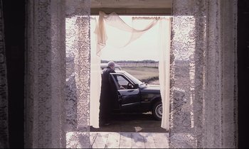Movie still from “The Sacrifice” (1986), directed by Andrei Tarkovsky – An older man sitting in a car in a doorway; Wide shot, Low angle