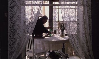 Movie still from “The Sacrifice” (1986), directed by Andrei Tarkovsky – A man sitting at a table with a wine glass; Wide shot, High angle