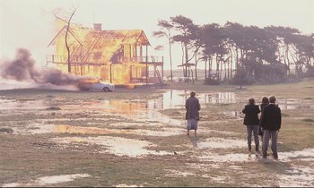 Two people walking through a flooded field near a house
