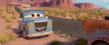 Movie still from “Cars 2” (2011), directed by John Lasseter – A blue truck is parked on the side of the road; Wide shot, Low angle