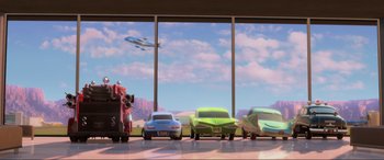 Movie still from “Cars 2” (2011), directed by John Lasseter – A group of cars parked in front of a window; Wide shot, Low angle