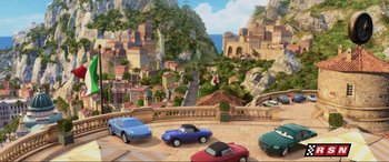 Movie still from “Cars 2” (2011), directed by John Lasseter – A painting of a street scene with cars parked on the side of the road; Extreme Wide shot, High angle