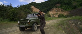 Movie still from “Carter” (2022), directed by Jung Byung-gil – A woman in a military uniform taking a picture in front of a truck; Medium shot, Low angle