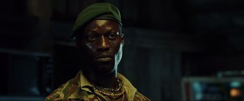 Movie still from “Casino Royale” (2006), directed by Martin Campbell – A man wearing a green hat and a camouflage jacket; Close Up shot, Low angle