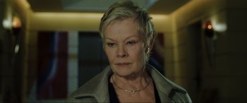 Movie still from “Casino Royale” (2006), directed by Martin Campbell – An older woman with short blonde hair wearing a jacket; Close Up shot, Low angle