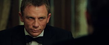Movie still from “Casino Royale” (2006), directed by Martin Campbell – A man in a suit and bow tie looking into the camera; Close Up shot, Over the shoulder angle