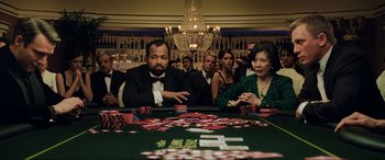 Movie still from “Casino Royale” (2006), directed by Martin Campbell – A group of people sitting around a table with cards; Medium shot, Over the shoulder angle
