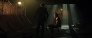 Movie still from “Casino Royale” (2006), directed by Martin Campbell – A man sitting on a chair next to another man in a dark room; Wide shot, High angle