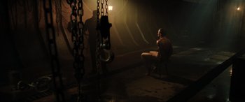 Movie still from “Casino Royale” (2006), directed by Martin Campbell – A man sitting on a chair next to another man in a dark room; Wide shot, High angle
