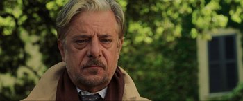 Movie still from “Casino Royale” (2006), directed by Martin Campbell – An older man with a beard and mustache wearing a coat and tie; Close Up shot, Over the shoulder angle