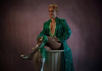 A man sitting on top of a barrel wearing a green outfit