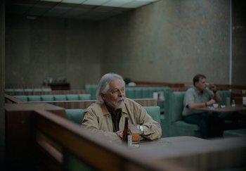 An older man sitting at a table with a bottle of beer
