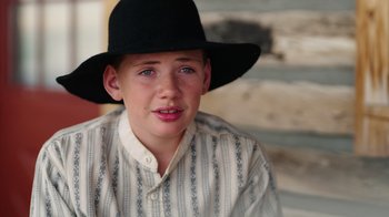 Movie still from “Catch the Bullet” (2021), directed by Michael Feifer – A young boy wearing a black hat and a white shirt; Close Up shot, Over the shoulder angle