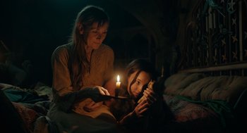 A woman and a girl sitting on a bed looking at a book