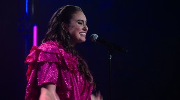 Movie still from “Catherine Cohen: The Twist...? She's Gorgeous” (2022), directed by Steven Brill – A woman in a pink dress singing into a microphone; Medium shot, Low angle