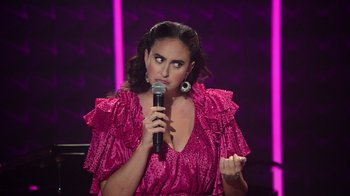 Movie still from “Catherine Cohen: The Twist...? She's Gorgeous” (2022), directed by Steven Brill – A woman in a pink dress is holding a microphone; Close Up shot, Over the shoulder angle