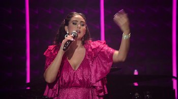 Movie still from “Catherine Cohen: The Twist...? She's Gorgeous” (2022), directed by Steven Brill – A woman in a pink dress singing into a microphone; Medium shot, Low angle