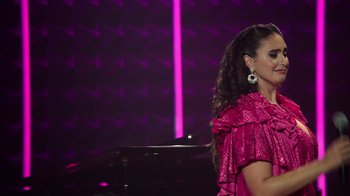 Movie still from “Catherine Cohen: The Twist...? She's Gorgeous” (2022), directed by Steven Brill – A woman in a pink dress standing in front of a piano; Medium shot, Low angle