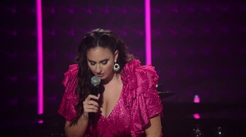 Movie still from “Catherine Cohen: The Twist...? She's Gorgeous” (2022), directed by Steven Brill – A woman in a pink dress holding a microphone; Medium shot, High angle
