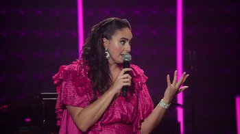 Movie still from “Catherine Cohen: The Twist...? She's Gorgeous” (2022), directed by Steven Brill – A woman in a pink dress is holding a microphone; Close Up shot, Over the shoulder angle